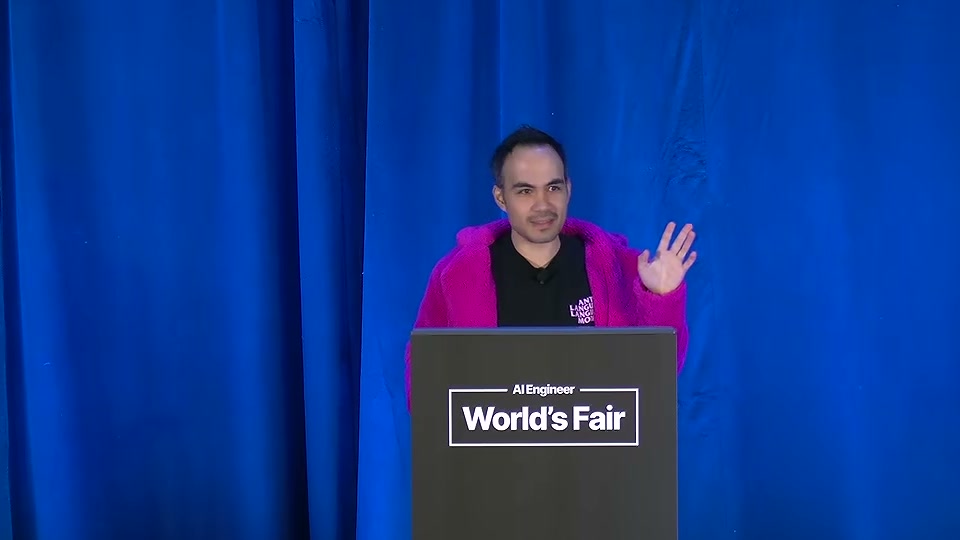 파란 커튼 앞 연단에 선 Diogo Almeida가 청중에게 손을 들어 보이고 있다. 연단에는 AI Engineer World's Fair 로고가 붙어 있다.